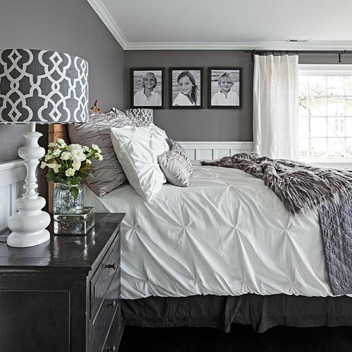 pilka siena su nuotraukomis baltame ir pilkame miegamajame, geometrinė šviestuvo lemputė juodoje lovoje