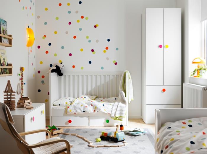 lepa stenska dekoracija s polka pikami, siva preproga, otroška posteljica in bela garderobna omara, gugalnik, bela komoda, rumena stenska svetilka