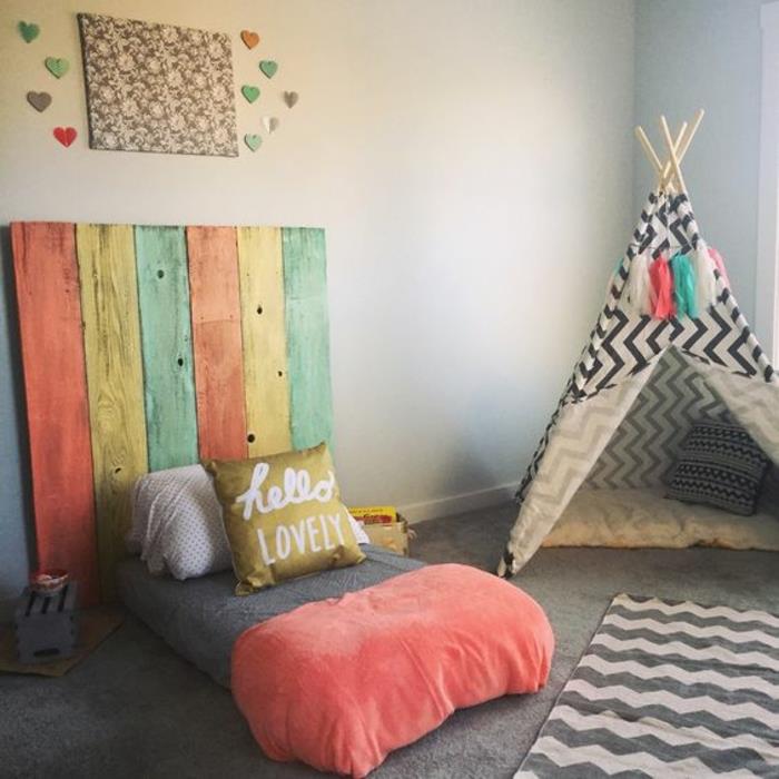 šviesiai pilka siena, Montessori kūdikio lova, spalvota medinė lentų galvūgalis, pilkas kilimas, vaiko titpi, Montessori metodas vaikų miegamojo išdėstymas