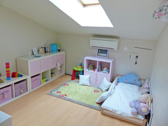 podstrešna soba, otroška posteljica brez rešetk, odlagalne enote v rožnati in beli barvi po celotni dolžini ene od sten, veliko okno na strehi, rožnata preproga in mignoneta z majhnimi cvetovi