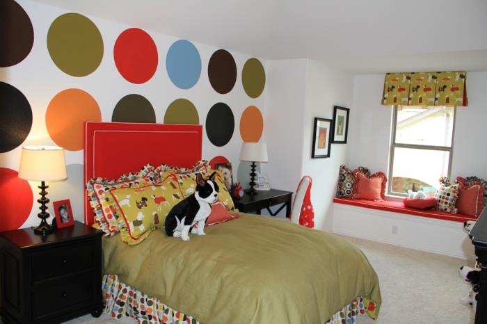 dekor spalnice najstnice, bela stena z velikimi rdečimi, oranžnimi, zelenimi, modrimi in črnimi pikami, dekor spalnice najstnice, ogrinjalo za posteljo, rdeče in belo vzglavje