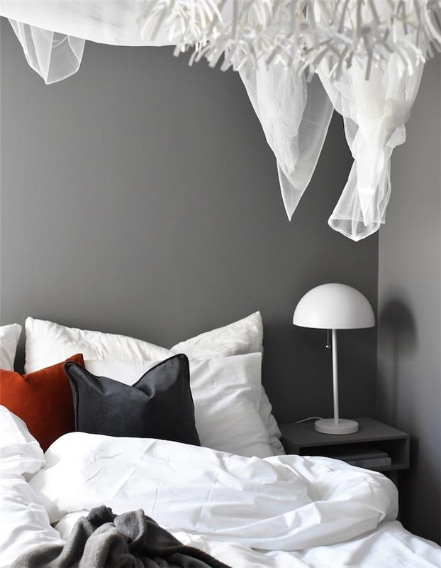 dekor glavne spalnice s sivimi stenami in sivo, belo in rdečo posteljnino, nočna svetilka preprostega dizajna