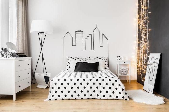 sivo -beli model spalnice, grafična risba na steni, črno -belo posteljno perilo, bela komoda, svetel parket, svetel girland, hygge trend