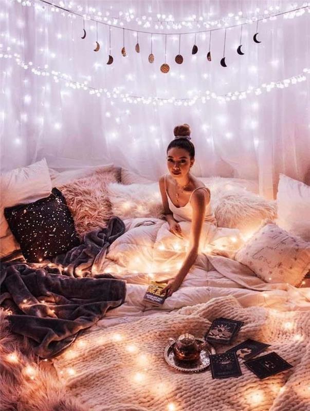 svajonių miegamojo dekoras su itin jaukia lova su krūva minkštų pagalvėlių ir visų rūšių šiltais metimais bei antklodėmis, lengva girlianda, skirta papuošti baldakimą