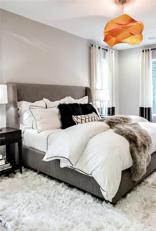 modernus miegamojo dekoras, pilka lova, oranžinė origami lubų lempa, purus baltas kilimas, šviesiai pilki sienų dažai