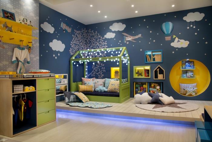 montessori pohištvo, postelja iz koče montessori v lesu, pobarvano v zeleno, stene pobarvane v račjo modro, z vzorci belih oblakov in barvitimi baloni na vroč zrak v pastelno modri in beli barvi