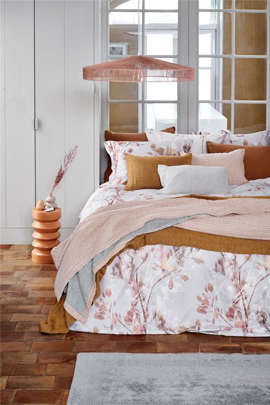 roza in bela spalnica s parketom in oranžnimi sestričnami na postelji, pokrita s cvetlično odejo