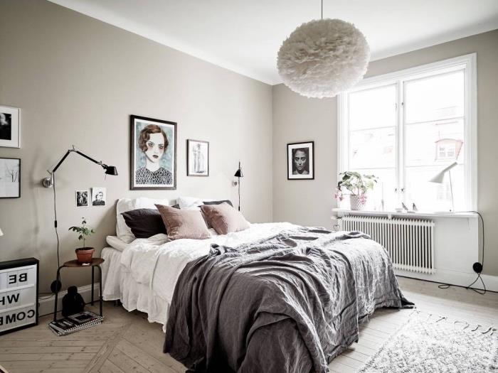 Yatak odasında İskandinav dekorasyon fikri, pembe minderli gri ve beyaz nevresimler, hafif parke, halı ve gri duvar, kadın portre dekorasyonu