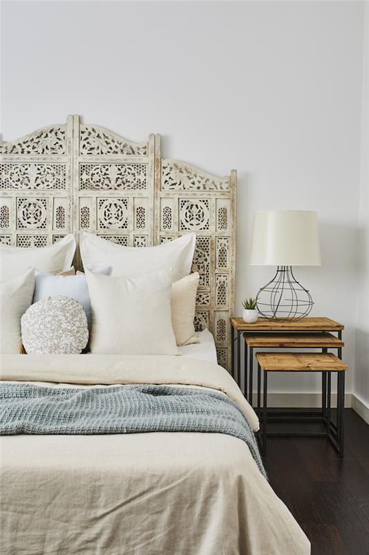 bohemiško stiliaus miegamasis baltos galvūgalio baltos pagalvėlės smėlio ir mėlynos spalvos užvalkalai naktinis stalas iš medžio ir metalinės baltos sienos