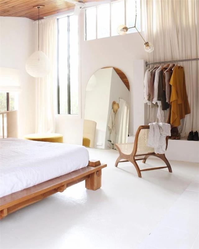 Spalnica v japonskem slogu v beli odprti garderobi lesena postelja in bela žimnica veliko ogledalo beli obesek svetlo nizka bela tla