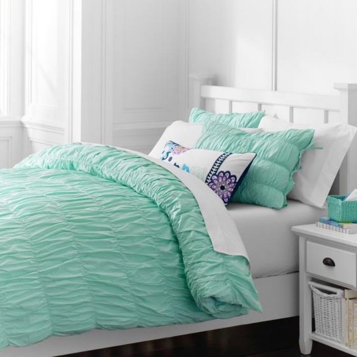 visiškai balta miegamojo idėja su keliais pastelinės žalios spalvos atspalviais ant patalynės, balta naktinio staliuko idėja su įmontuota saugykla