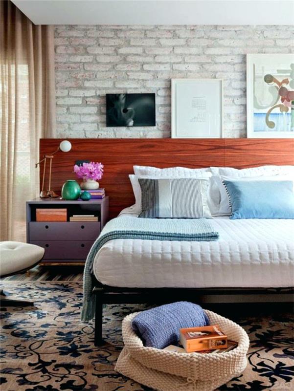 Zen dekor za spalnico s cvetlično preprogo, lesenim vzglavjem, opečnim ozadjem, lila posteljo