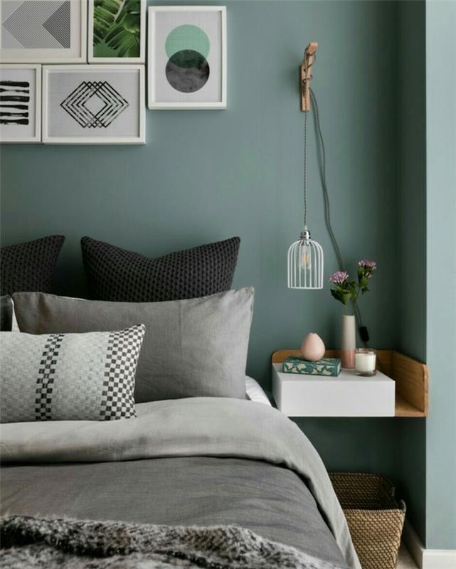 temno sive zelene stene v oblikovalski spalnici za odrasle, sivo -črna posteljnina, lesena nočna omarica, pritrjena na steno, stena z okrasnimi okvirji na vzglavju