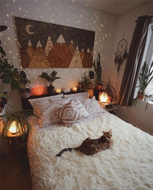 miela katė ant lovos, padengtos balta avikailiu, daržovių galvūgalio apdaila, kalnų kraštovaizdžio piešinys ant skydelio, svajonių gaudyklės sienų apdaila
