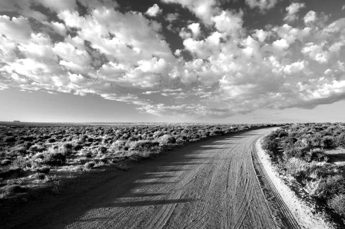 črno -bela fotografija poti v puščavi, ki se izgubi na obzorju, pod očmi plesnih oblakov