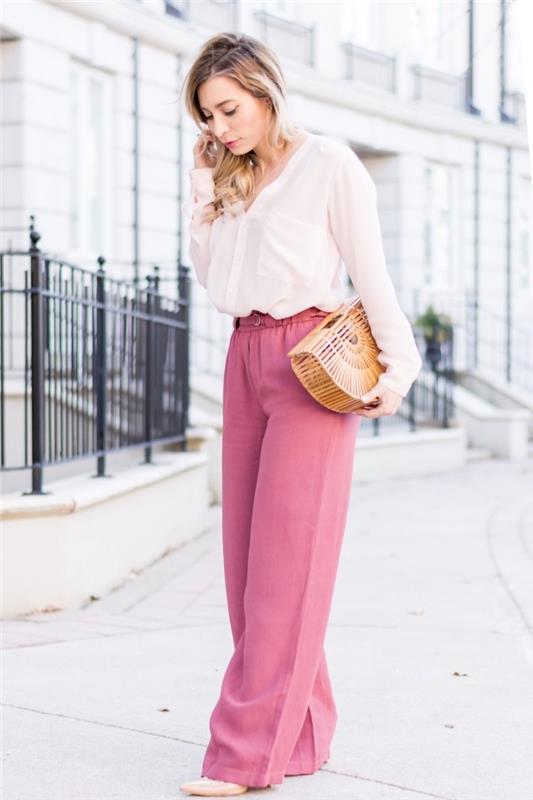 elegantiška moteris atrodo plačiomis rožinėmis kelnėmis ir baltais marškiniais, prie kurių pridedama madinga rankinė ir smėlio spalvos bateliai