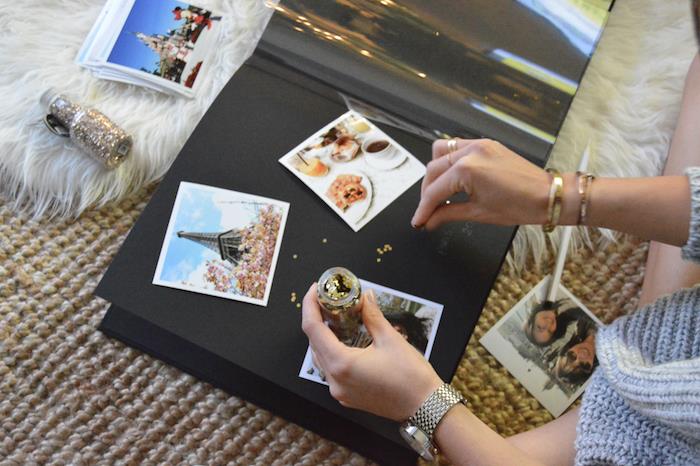 Črni kartonski papir, potovalne fotografije v Parizu, ženska, ki okoli fotografij vbrizga iskrice, album z beležkami, kako sami narediti potovalni beležko