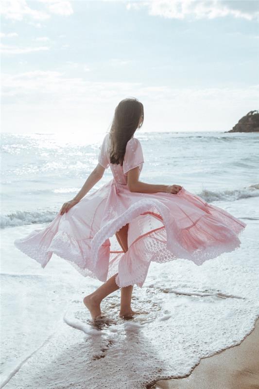 Šviesiai rožinė ilga suknelė moteris prie paplūdimio kojų vandenyje