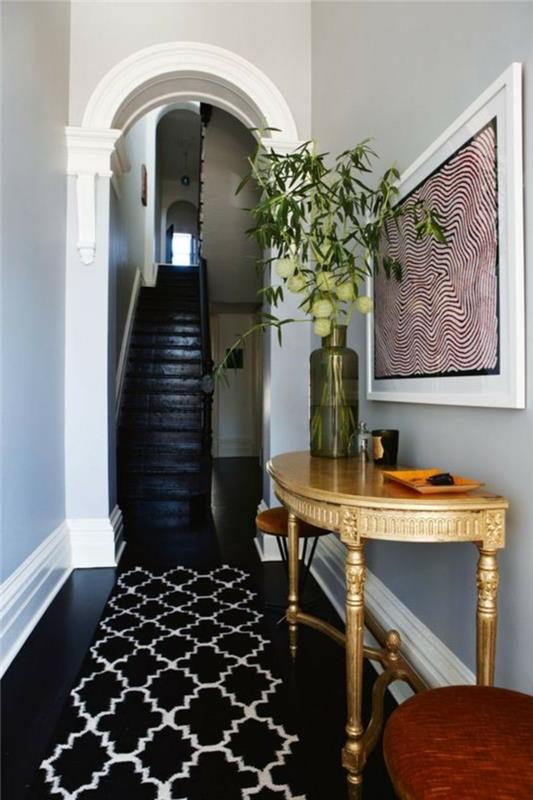 Juodos grindys ir pilkos sienos, siaura prieškambario spintelė, paprasta ir efektyvi apdaila, vaza su gėlėmis ant pusapvalio stalo