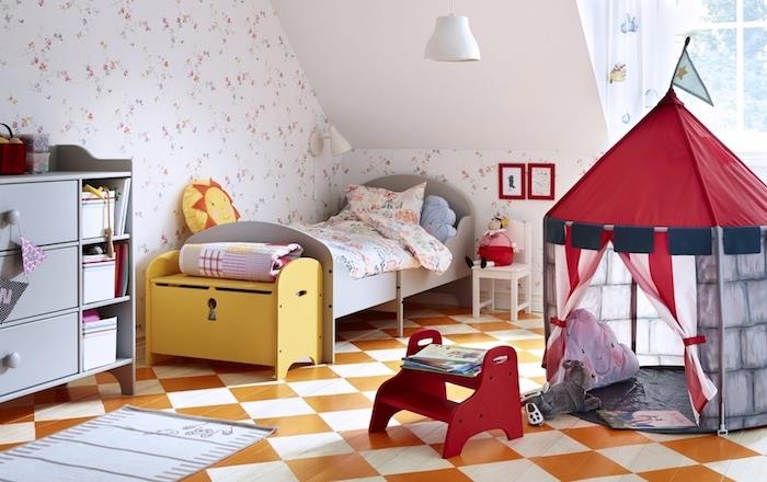 vaikų kambarys po šlaitu su žema lova, komoda su mažai atidaryta saugykla, oranžinės ir baltos plytelės, vaikų „teepee maisonette“, gėlių rašto tapetai