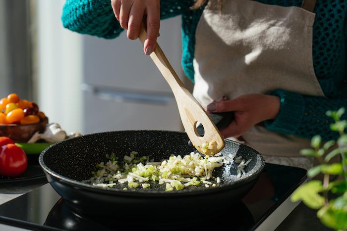 siyah sos tavasında pişmiş, tahta spatula ile karıştırılmış kereviz ve soğan, domates çorbası tarifi