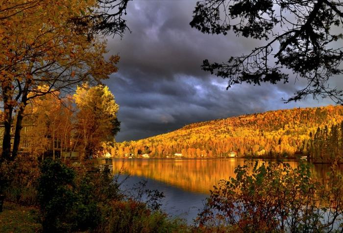 nevihtno nebo, rečni breg, ki ga zlati sonce, drevesa z rumenim listjem, jesenska pokrajina