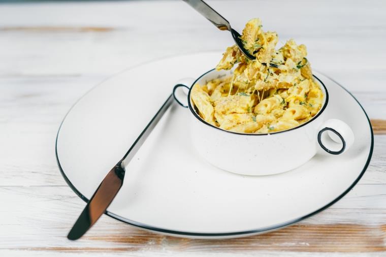 ciotola con penne integrali al formaggio cheddar condire la pasta con foglie di basilico