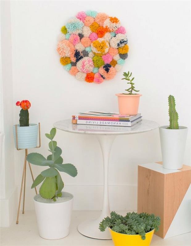 birbirine yapıştırılmış çok renkli ponponlardan yapılmış yuvarlak duvar dekorasyonu, kolay sanatlar ve el sanatları, küçük beyaz bir masanın üzerine asılı, ahşap tabure ve saksı bitkileri
