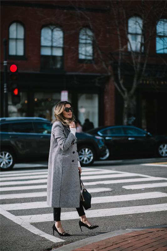 ženska, ki hodi po ulici, napoved modnega trenda 2019, oblečena v črne hlače in pete, v črno -belem dolgem kariranem plašču