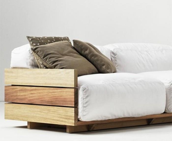 trys smėlio spalvos pagalvės, dekoruojančios pasidaryk pats sofą, pagamintos iš medinių padėklų, su beveik baltomis sofos pagalvėlėmis, baltomis grindimis ir fonu