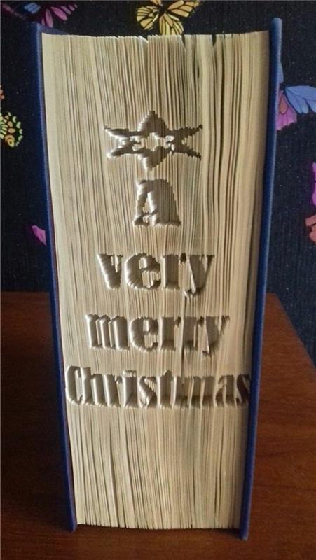 zaprta knjiga s temno modrimi trdimi platnicami, z zvezdico in izrazom zelo vesel božič, vklesan na njenih straneh