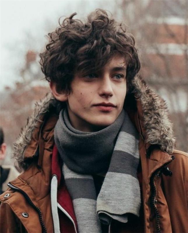 berniuko šukuosena su šiek tiek garbanotais vidutinio ilgio plaukais, negražus stiliaus efektas, žiemiška išvaizda, ruda striukė, vyriška skara