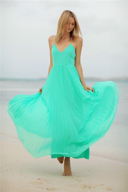 mados idėja moteriai paplūdimyje su ilga tekančia suknele su ryškiai žalios spalvos v formos iškirpte su aukso spalvos karoliais
