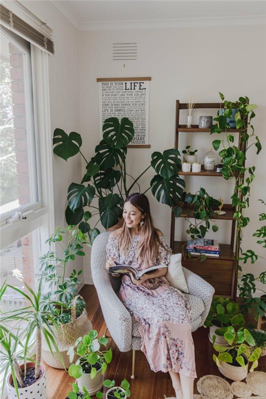 Moteris skaito knygą savo bohemiško stiliaus skaitymo kampe, žali augalai, nedidelis 40m2 buto išplanavimas, šiuolaikiška buto dekoravimo idėja