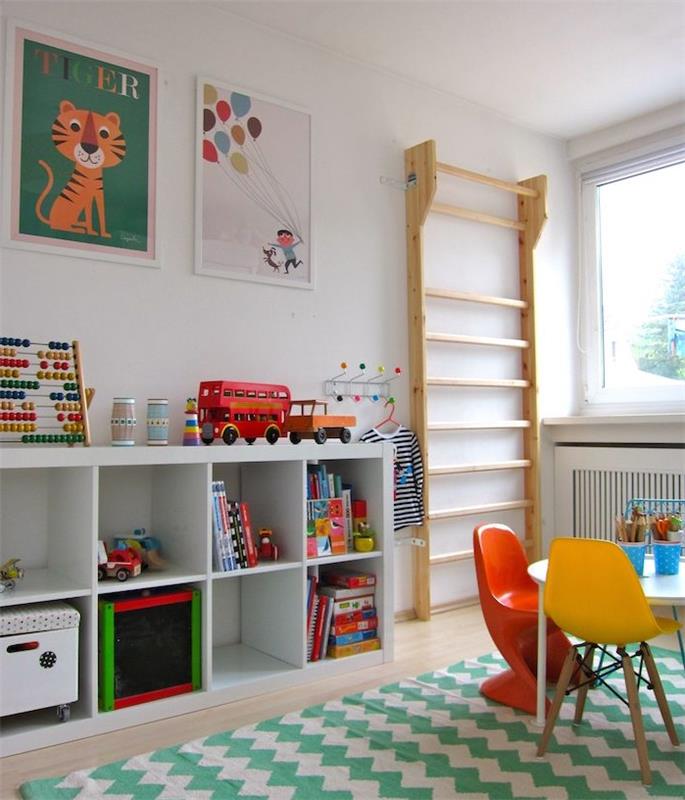 Baltoji „Kallax“ lentyna vaiko kambariui, „Montessori“ pedagogika namuose, žaliai baltas „Chevron“ kilimas, žemas stalas ir kėdės, vaikų žaislai ir plakatai ant sienos