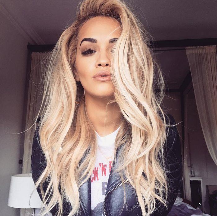 platinos blondinės spalvos rita ora ilgi banguoti plaukai su apimties odine striuke balti marškinėliai