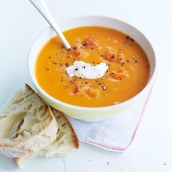 Ricetta vellutata di zucca, ciotola con minestra e panna, pezzettini di pane vicino alla ciotola