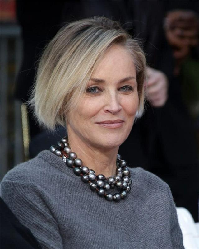 Sharon Stone kvadratinis kirpimas, tekantys peleniniai šviesūs plaukai, pilkas megztinis