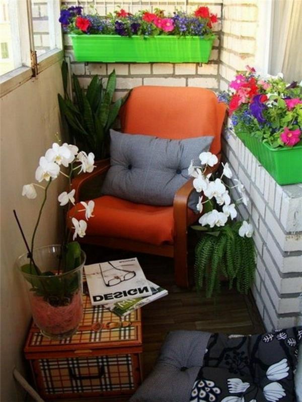 leseni balkonski naslanjač z oranžno sedežno blazino in sivo okrasno blazino, lesena obloga za teraso, majhna skrinja, cvetlične škatle z barvitimi cvetovi