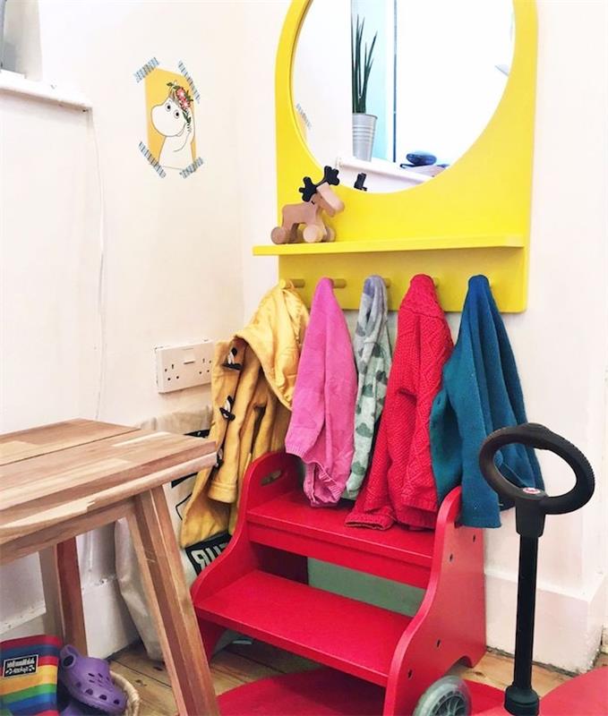 Vaikų įėjimas su mažu raudonu vaikišku suoliuku, geltonu veidrodžiu ir žemu paltu