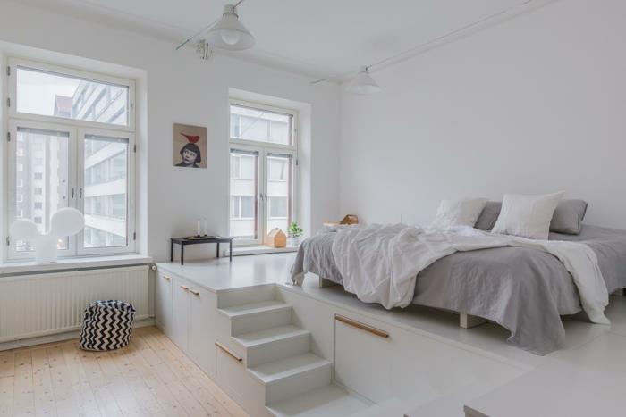 nedideli balti laiptai miegamajame, pilka ir balta lova, lentos grindys, indistriel dizaino lempa