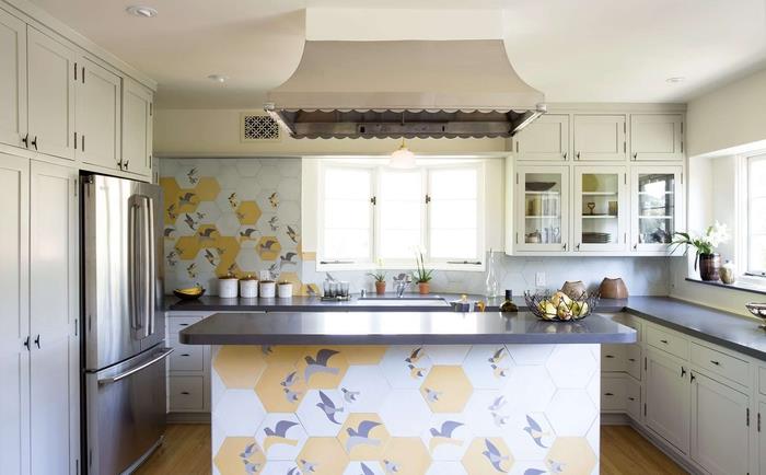 Backsplash duvarında ve orta adanın ön tarafında kuş motifli altıgen çimento karolarla canlandırılan işlevsel ve samimi beyaz ve gri mutfak