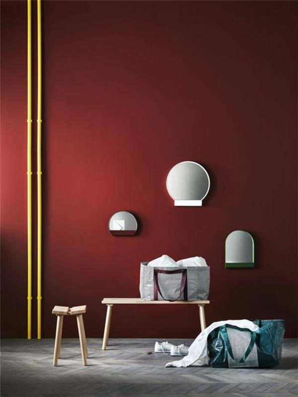 įėjimo idėja su rubino raudonos spalvos sienomis ir geltonos spalvos elementais, parketu padengta tamsiai ir šviesiai pilka spalva, suoliukas šviesiai bis, maža kėdė iš šviesios medienos, trys sieniniai šviestuvai baltos spalvos, apvalios formos