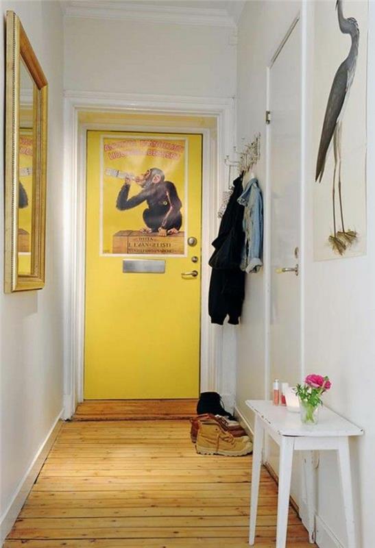 prieškambario dekoras, baltos sienos, geltonos durys, geltonas žalios medienos parketas, stačiakampis stalas, nudažytas baltai, didelis kvadratinis veidrodis su auksiniu rėmu, pastatytas priešais baltas duris