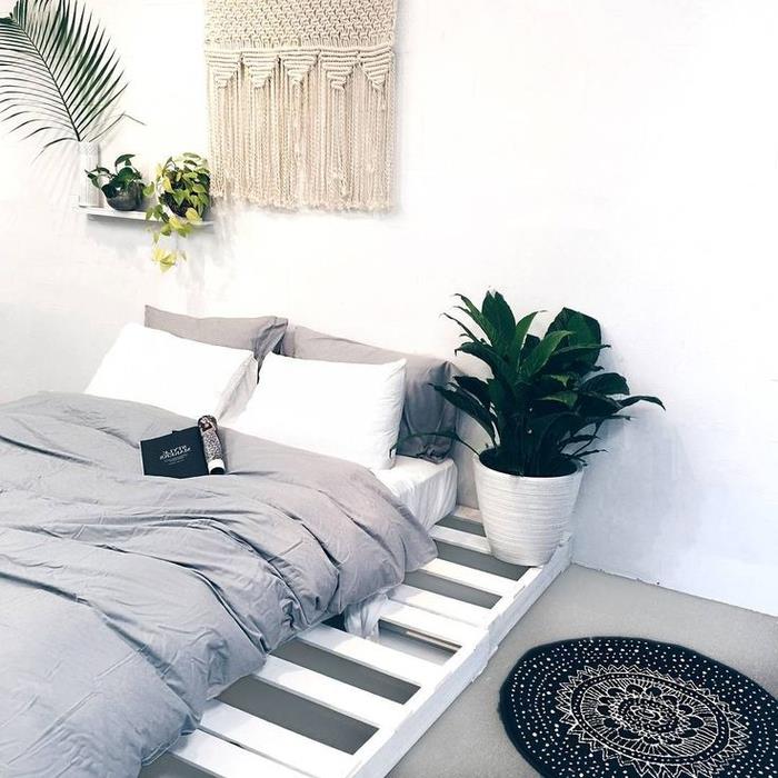 şilteyi aşan basit bir palet bazalı yatak ile bohem şık bir ambiyansa sahip beyaz ve gri bir yatak odası