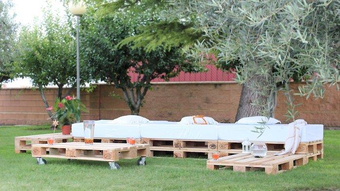 Bir bahçede çimenlerin üzerinde tekerlekli palet kanepe ve palet sehpa ile palet bahçe mobilyaları modern modeli