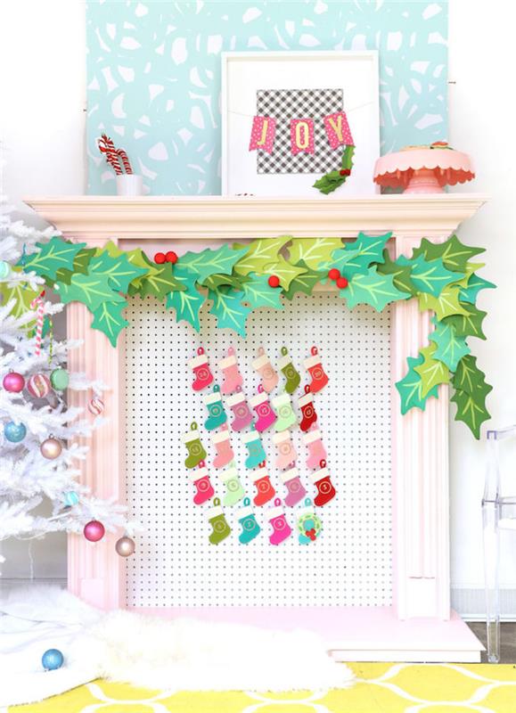 mažos kalėdinės kojinės pakabintos ant skylėtos plokštės priešais dekoratyvinį kalėdinį židinį, bliuzo lapų girliandą
