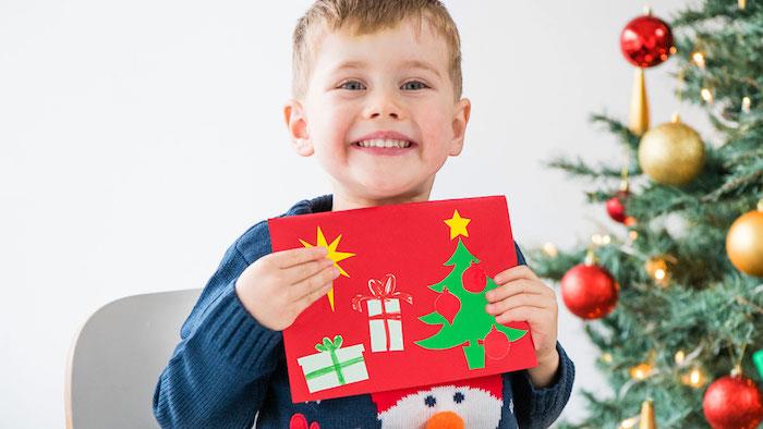 Vaikų darželio Kalėdų atviruko idėja „scrapbooking“ iš raudono popieriaus, papuošto eglutės raštais ir popierinėmis dovanomis