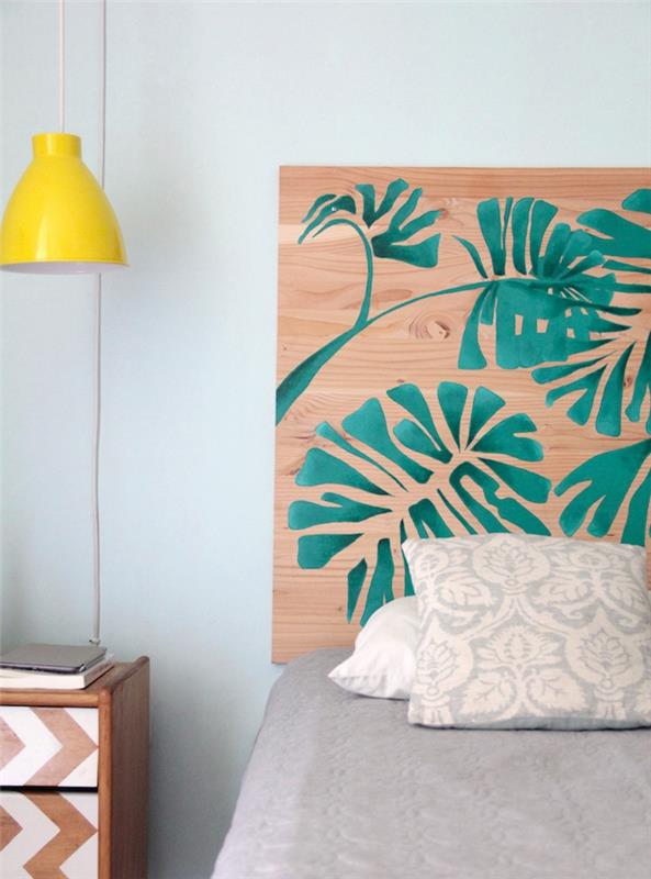 Vzglavnik iz vezanega lesa, okrašen z zelenimi palmovimi listi, sivim posteljnino, leseno nočno omarico, okrašeno z belo barvo