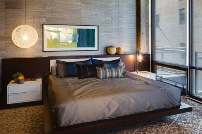 zen postelja, lesena ploščad, bele nočne omarice, okrogla viseča stropna svetilka, nevtralna preproga